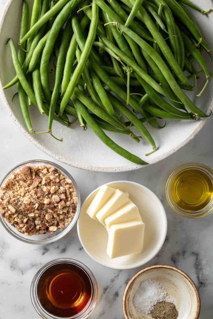 Roasted Green Beans Recipe Fresh green beans on a white plate next to butter and olive oil.