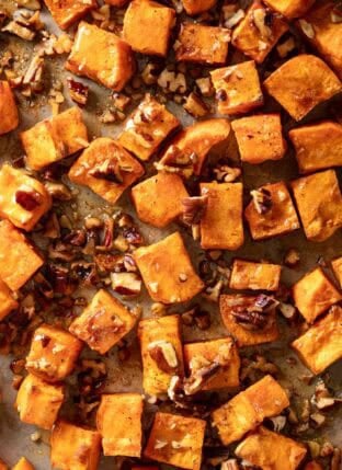 Oven Roasted Sweet Potatoes with maple syrup and pecans on a baking sheet.