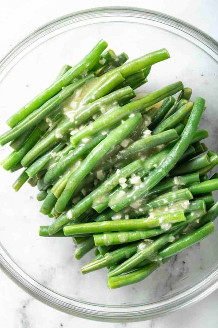 How to Steam Green Beans Steamed Green Beans in a glass bowl with garlic butter poured over the top.