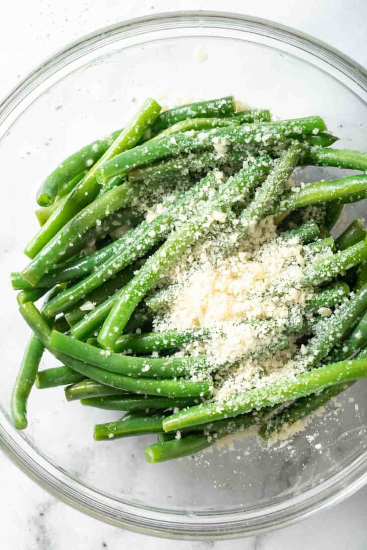 How to Steam Green Beans Steamed green beans tossed with parmesan cheese in a clear glass bowl.