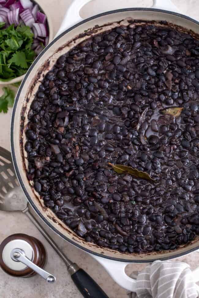 A large white pot filled with cooked Cuban black beans.