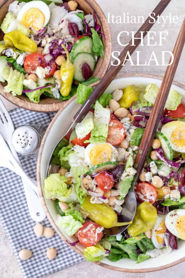Two wooden bowls filled with romaine lettuce, hardboiled eggs, almonds and tomatoes. A pair of salad servers in one bowl.