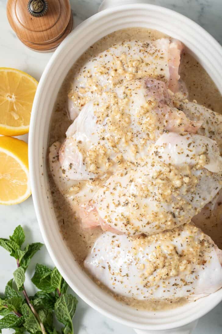 Greek Seasoning Mix Marinating chicken in a shallow white oval bowl.
